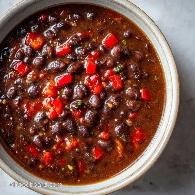 A deep bowl of velvety dark soup garnished with diced avocado, red onion, and a wedge of bright lime on the side.