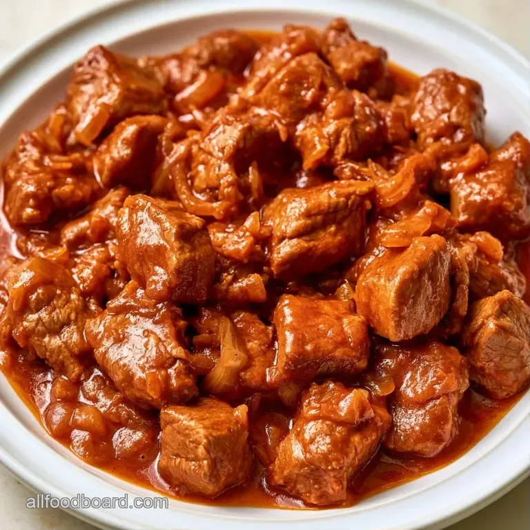 Steaming bowl of tender beef chunks in a glossy crimson gravy, garnished with fresh parsley and creamy swirls.