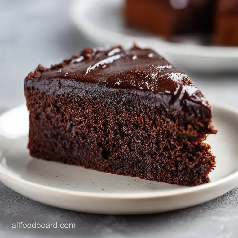 Slice of moist chocolate cake with glossy ganache, adorned with fresh raspberries and a sprig of mint.